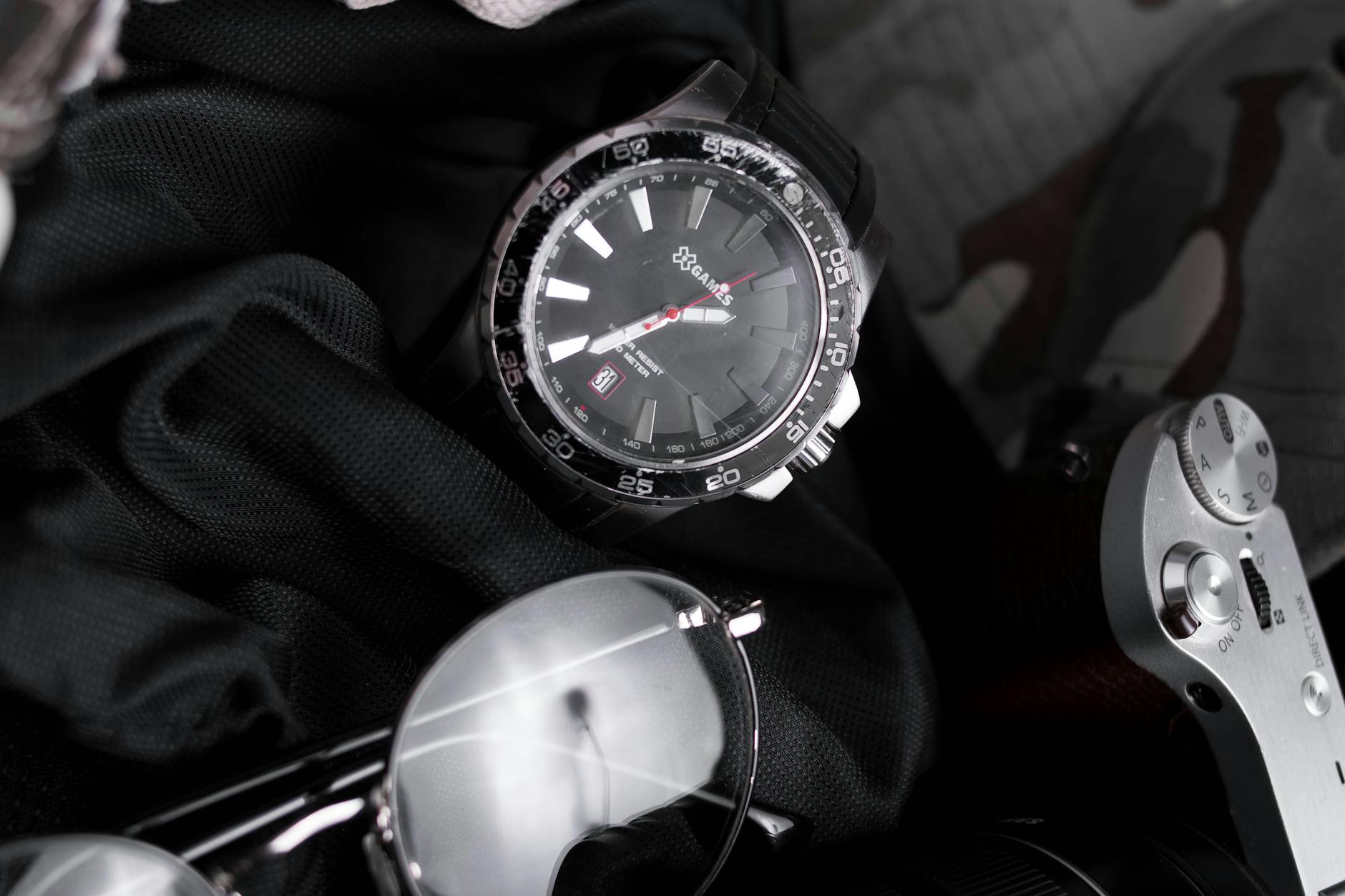 Close-up of a stylish black wristwatch with sunglasses and a camera.